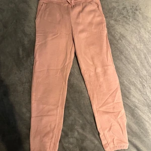 Rosa mjukisbyxor från Reaction - Mysiga rosa mjukisbyxor från Reaction med resår och snörning i midjan. Byxorna har en relaxed passform och är tillverkade i mjukt bomullsmaterial, perfekta för chill dagar. Fickor på sidorna och elastiska benslut för extra komfort.