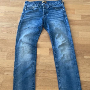 Slim fit jeans från Jack & Jones - Snygga blå slim fit jeans från Jack & Jones, modell Glenn. Jeansen har klassisk femficksdesign, normal midja och lätt slitna detaljer framtill för en cool look. Tillverkade i stretchig bomull för skön passform.