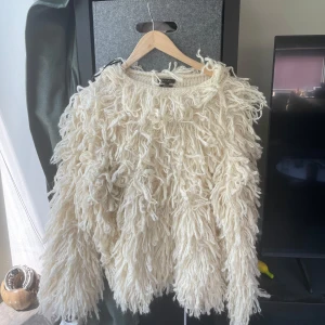 Krämvit fluffig stickad tröja Massimo Dutti - Aldrig använd! Superunik krämvit stickad tröja från Massimo Dutti med långa, fluffiga garnöglor över hela tröjan. Den har rund hals och långa ärmar, perfekt för dig som vill sticka ut med en cozy statement piece. Materialet känns mjukt och värmande.