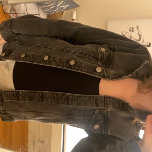 Svart jeansjacka från Gina Tricot - Säljer en svart jeansjacka från Gina Tricot med klassisk design och silverfärgade knappar. Jackan har två bröstfickor med lock och knäppning framtill. Perfekt att slänga över en t-shirt eller hoodie.