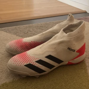 Adidas Predator fotbollsskor i vitt och rött - Säljer ett par Adidas Predator fotbollsskor i vitt med svarta ränder och röda detaljer. Skorna har en strumpliknande passform utan snörning och mönstrad sula för bra grepp på planen. Perfekta för dig som vill sticka ut på fotbollsplanen! Ja har köpte de för flera år sen men de va liten och tills nu har jag inte använt de och det är bättre bara att sälja den men den är bara lite smutsig för att den har legats i en papperspåse i källaren.
