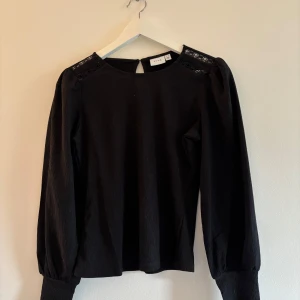 Svart blus med detaljer  - Säljer en svart blus från vila med långa ärmar. Blusen har en knapp i ryggen. Säljer då den inte passar och där av har jag inte möjlighet att prova den på. Kan fixa bild från hemsidan eller liknande. 