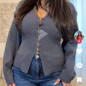 Grå kofta med knappar - Säljer en grå kofta med v-ringning och dekorativa knappar framtill. Tröjan har lång ärm och är i ett mjukt material som passar perfekt till jeans. Enkel och stilren design. Köpt på gina tricot,använd få gånger