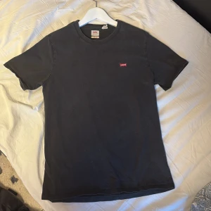 Svart t-shirt från Levi's - Klassisk svart t-shirt från Levi's med liten röd logotyp på bröstet. Enkel och stilren design med rund hals och korta ärmar. Perfekt basplagg till garderoben.