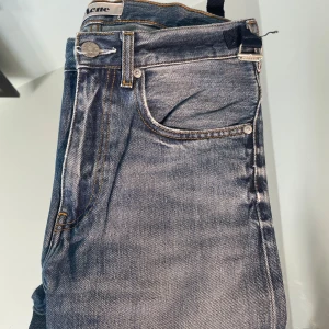 Blå jeans från Acne Studios - Säljer ett par klassiska blå jeans från Acne Studios med fem fickor och raka ben. Jeansen har normal passform och är tillverkade i slitstarkt denim med snygga kontrastsömmar. Perfekta för en stilren och avslappnad look.
