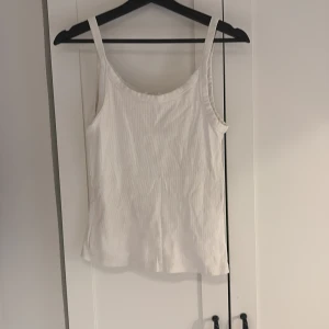 Vit ribbad linnetopp - En klassisk vit ribbad linnetopp med smala axelband. Perfekt att styla till jeans eller kjol för en enkel och fräsch look. Mjuk och bekväm med stretchigt material. Hör gärna av dig vid intresse