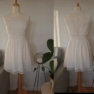 Vit spetsklänning från Vero Moda - Superfin vit klänning från Vero Moda med spetsdetaljer upptill och i ryggen. Klänningen är ärmlös, har markerad midja och lätt utställd kjol. Dragkedja i sidan och diskret prickigt mönster i tyget. Perfekt för sommarens tillfällen!