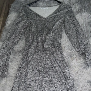 Zebramönstrad långärmad klänning från Sinsay - Säljer en långärmad klänning från Sinsay med zebramönster i svart och vitt. Klänningen har v-ringad hals och är figurnära upptill med lätt utställd kjol. Perfekt för dig som gillar djurmönster och vill sticka ut.