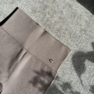 Beige ribbade leggings med hög midja från DOM - Säljer ett par beige ribbade leggings med hög midja. De är stretchiga i mjukt material för extra komfort. Perfekta för en avslappnad stil eller till träning. Liten söt berlockloga framtill vid linningen.