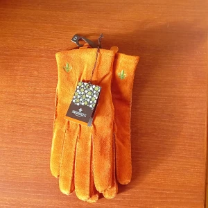 Orange skinnhandskar från Morris - Snygga orangea handskar i skinn från Morris med broderad logga på ovansidan. Handskarna har en klassisk design och storlek 8.5, vilket motsvarar herr M men passar som S. Perfekta för att ge din outfit en färgklick.