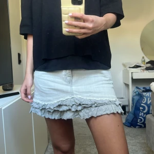 Ljusgrå jeanskjol med volangkant - Säljer ett par ljusgrå jeansshorts med volangkant nertill. Shortsen har klassisk femficksdesign och knappgylf. Perfekta för sommardagar när du vill ha något unikt och snyggt.