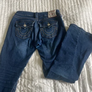Blå jeans från True Religion - Säljer ett par klassiska blå jeans från True Religion med deras ikoniska bakfickor och kontrastsömmar. Jeansen är både insydda och uppsydda så passar bäst storlek 26 även fast de är köpta i 27