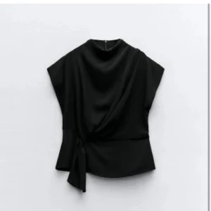 Svart knyttopp från Zara - Säljer en svart omlottopp från Zara i storlek XS. Toppen har korta ärmar, hög hals och en snygg knytdetalj i midjan som ger en elegant siluett. Perfekt att styla med både jeans och kjol.