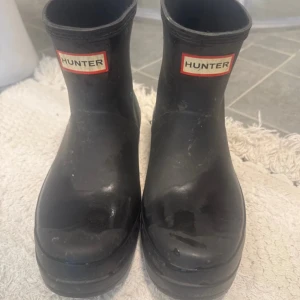 Svarta gummistövlar från Hunter - Säljer ett par klassiska svarta gummistövlar från Hunter. De har en låg modell med rund tå och tydlig Hunter-logga både fram och bak. Perfekta för regniga dagar och enkel att matcha med olika outfits.