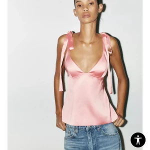 Rosa satinlinne med knytband - Säljer ett ljusrosa linnetopp i satin med djup v-ringning och breda axelband som knyts till rosetter. Toppen har öppen rygg och en figurnära passform. Perfekt för sommardagar och snygg till jeans eller kjol.