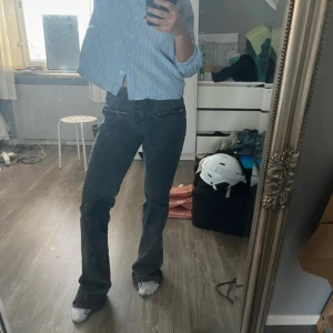 Svarta bootcut jeans med dragkedjedetaljer - Säljer ett par svarta bootcut jeans med låg midja och dragkedjor framtill. Jag är 160cm och de sitter längre på mig. Storlek S