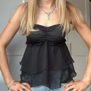 Svart volangig tubtopp - Säljer en svart tubtopp med flera lager volanger och lätt rynkning vid bysten. Toppen är axelbandslös och har en luftig, flowy känsla tack vare det tunna tyget. Perfekt att styla med jeans eller kjol för en trendig look. ⊹ jag är 173cm & stl S/36/28 för referens ⊹ läs POLICY (i gillade inlägg) innan köp ⊹ använd gärna ”Köp” ⊹ 