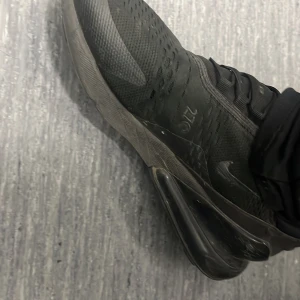 Svarta Nike Air Max 270 sneakers - Säljer ett par svarta Nike Air Max 270 sneakers med synlig luftbubbla i sulan och stickad ovandel. Skorna har snörning och en sportig design som passar perfekt till vardags och träning.