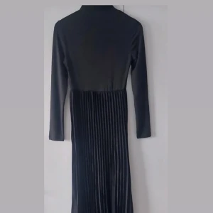 Svart långklänning med plisserad kjol - Säljer en svart långklänning med långärmad överdel och plisserad kjol. Klänningen har en elegant och stilren design, perfekt för speciella tillfällen. Materialet känns mjukt och följsamt.Passar även 36