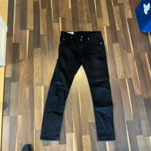 Svarta jeans från J.Lindeberg - Snygga svarta jeans från J.Lindeberg med klassisk femficksdesign och raka ben. Perfekta för dig som vill ha en stilren och tidlös look. Byxorna har silverfärgade nitar och knappdetaljer.
