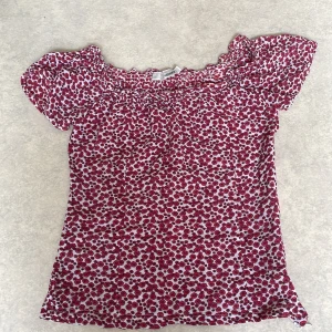 Röd blommig blus från Hennes - Söt blommig blus från Hennes i rött och vitt. Blusen har korta ärmar, smock upptill och volangdetalj vid halsringningen. Tillverkad i mjuk viskos som känns skön mot huden.