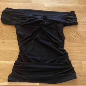 Svart offshoulder topp från Gina Tricot - Säljer en svart offshoulder topp från Gina Tricot i storlek XXS. Toppen har åtsittande passform och snygga rynkade detaljer längs sidorna och framtill. Perfekt för dig som gillar en stilren och trendig look.