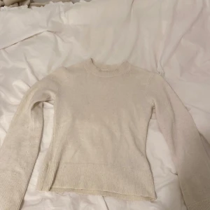 Vit stickad tröja från H&M - Säljer en enkel och stilren vit stickad tröja från H&M i storlek XS. Tröjan har långa ärmar, rund halsringning och bred ribbad kant vid ärmslut och nederkant. Perfekt basplagg till garderoben. Den är lite sliten på ena armen längst ner som syns på bilden