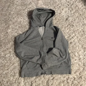 Grå hoodie från Polo Ralph Lauren - Säljer en klassisk grå hoodie från Polo Ralph Lauren med dragkedja och huva. Tröjan har två fickor framtill och en liten broderad logga på bröstet. Perfekt för en avslappnad stil.