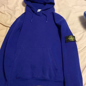 Blå hoodie från Stone Island - Säljer en blå hoodie från Stone Island med klassisk patch på vänster ärm. Tröjan har huva med dragsko och en stor magficka framtill. Perfekt för dig som gillar streetwear och vill ha något stilrent men ändå med tydlig logga. Passar 170 och under. Ni vet varför den är billig