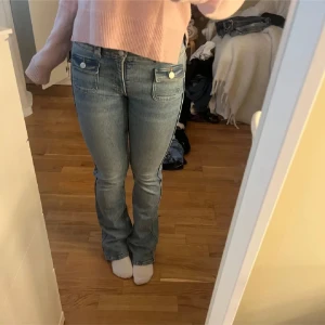Blå bootcut jeans med fickdetaljer - Säljer ett par blå bootcut jeans med två framfickor med lock och dubbla knappar i midjan. Säljs knappt längre. (Lånade bilder) skriv för bilder😇