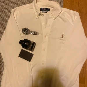 Vit skjorta från Polo Ralph Lauren - Klassisk vit skjorta från Polo Ralph Lauren med button-down krage och broderad logga på bröstet. Skjortan är i bomull och har långa ärmar samt knappar framtill. Perfekt för en clean och stilren look.