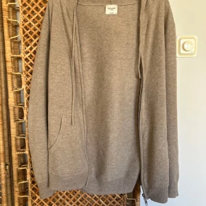 Beige hoodie i kashmir från John Henric - Mysig beige hoodie i kashmir från John Henric. Tröjan har dragkedja, huva och två fickor framtill. Perfekt för lager-på-lager och en avslappnad stil. Klassisk passform och mjukt material som känns lyxigt mot huden. Nästan helt perfekt skick men med ett litet smalt hål på den lägre delen. Skulle passa den lite mer bredaxlade personen. Ny pris: 2400, mitt pris: 1300