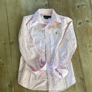 Rosa och vit randig skjorta från Ralph Lauren - Säljer en klassisk rosa och vit randig skjorta från Ralph Lauren i modellen Custom Fit. Skjortan är extremt stilren och perfekt för den kommande sommaren! Den är i väldigt fint skick och är i storlek xs😁 Säljer då den tyvärr är lite liten för mig😔skriv gärna om ni har några funderingar🤗🤗🤗