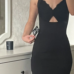 Svart tight klänning med öppen rygg - Säljer en svart tight klänning med smala axelband och snygg v-ringning framtill. Klänningen har en unik öppen rygg med korsade band och en liten cut-out detalj vid bysten. 