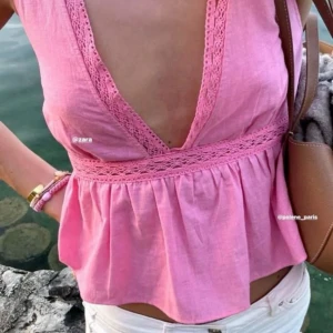 Rosa ärmlös topp med spetsdetaljer och knytning i ryggen - Säljer en söt rosa ärmlös topp från Zara med djup v-ringning och spetsdetaljer längs kanterna. Toppen har en markerad midja och knytning i ryggen för extra detalj. Perfekt för varma dagar!