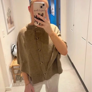 Beige stickad kofta med knappar - Säljer en beige stickad kofta med stora knappar framtill och ribbade detaljer vid hals och nederkant. Koftan har en lös passform och är perfekt för lager-på-lager-stil. Superenkel att slänga på sig över en t-shirt eller topp.