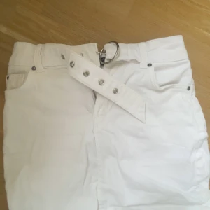 Vit jeanskjol med bälte från Bershka - Säljer en vit jeanskjol från Bershka med tillhörande bälte och silverfärgade detaljer. Kjolen har klassisk femficksdesign och är i en kort modell. Perfekt för dig som gillar en stilren och trendig look. Kontakta om du har frågor!