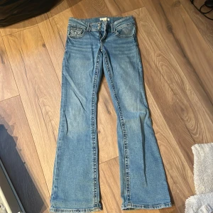 Blå bootcut jeans - Säljer ett par klassiska blå bootcut jeans med fem fickor och normal passform. Jeansen har en lätt tvättad look och är perfekta för dig som gillar en tidlös stil. Dragkedja och knapp framtill. Passar till det mesta!