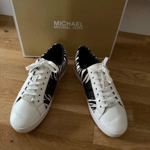 Michael Kors sneakers med zebramönster - Snygga sneakers från Michael Kors med zebramönstrade paneler i svart och vitt. Skorna har vita snören, vit sula och svarta detaljer på sidan. Perfekta för dig som vill sticka ut med ett djurinspirerat mönster och exklusiv känsla.
