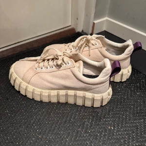 Eytys sneakers  - Säljer ett par vita sneakers från Eytys med mönstrad plattformsula och lila hälflik. Skorna har snörning och är tillverkade i canvasmaterial. Perfekta för dig som gillar en unik och trendig stil.