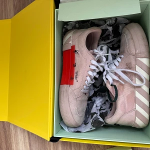 Beige Off-White sneakers med vita snören - Säljer ett par beige sneakers från Off-White med vita snören och ikoniska Off-White-pilar på sidan. Skorna har en vit och beige randig sula samt en röd tag på sidan. Perfekta för dig som gillar streetwear och vill sticka ut.