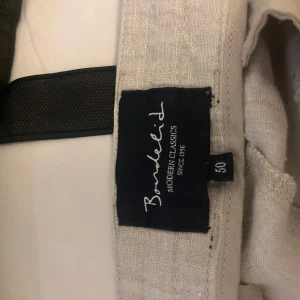 Beige linnebyxor från Bondelid - Säljer ett par ljusbeige linnebyxor från Bondelid, modell Modern Classics. Byxorna har normal passform, snörning i midjan och två bakfickor med knapp. Perfekta för varma dagar och en avslappnad stil. Finns ett litet hål på höger baksida, men inget större 