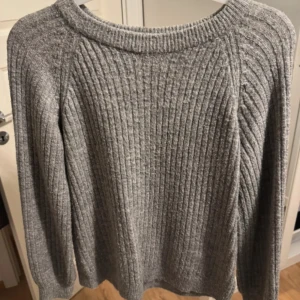 Grå ribbstickad tröja - Säljer en klassisk grå ribbstickad tröja med rund halsringning och långa ärmar. Perfekt för kyligare dagar och enkel att matcha med olika outfits.
