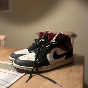Nike Air Jordan 1 Retro High OG svart/vit/röd - Säljer ett par Nike Air Jordan 1 Retro High OG i svart, vitt och rött. Klassisk high-top modell med svart swoosh, vit tå och sidor samt röda detaljer vid ankeln. Skorna har snörning och platt sula. Perfekta för dig som gillar streetwear och sneakers.