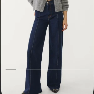 Mörkblå wide leg jeans med hög midja - Säljer ett par mörkblå jeans med hög midja och raka, vida ben. Jeansen har markerade sömmar framtill och klassiska fickor bak. Perfekta för en trendig och avslappnad look.