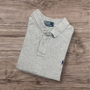 Ralph Lauren Piké - Ralph Lauren Pikétröja – Grå (L/XL)⚪👕  Säljer en klassisk och stilren grå piké från Ralph Lauren i storlek L/XL. Tillverkad i bekvämt material och passar perfekt både till vardags och mer uppklädda tillfällen. Tidlös modell med broderad logga.  ✅ Storlek: L/XL 📏 Mått: Längd 75 cm, armhåla till armhåla 70 cm, axel till axel 55 cm 🎨 Färg: Grå 👕 Modell: Pikétröja 🏷 Märke: Ralph Lauren 🛍 Nypris ca 1800 kr  📍 Finns för avhämtning i Linköping eller skickas mot fraktkostnad. 💬 Hör av dig vid intresse! 