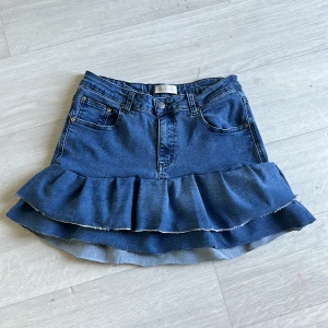 Jeanskjol med volang från Create Denim - Supersöt blå jeanskjol från Create Denim med volangkant nertill. Perfekt för dig som gillar en trendig och avslappnad stil. 