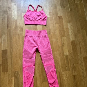 Rosa  träningstights med matchande topp  - Säljer ett par rosa  tights med hög midja och snygga meshdetaljer samt matchande topp. Tightsen/toppen är stretchiga och sitter tight, perfekta för gymmet eller löprundan. Materialet är mjukt och andas bra. Matcha med sport-bh för en komplett träningslook.