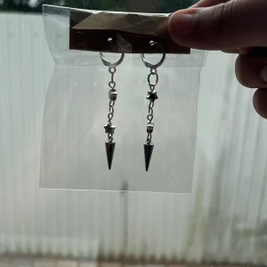 Silvriga örhängen med stjärnor och spikes - Säljer ett par coola silvriga örhängen med kedjor, små stjärndetaljer och spetsiga spikes längst ner. Perfekta för dig som gillar edgy och unik stil. Hängande modell som verkligen sticker ut.