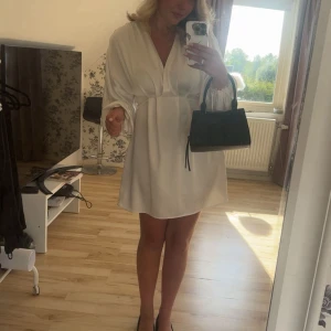 Vit omlottklänning med v-ringning - Superfin vit satin kortklänning med v-ringning och omlottkänsla. Långa ärmar med lätt puff och lös passform som ger en chill men ändå elegant vibe. Perfekt för sommarens alla tillfällen!